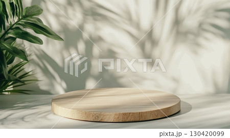 Empty round wooden podium on table illuminating by sunlight with green plant and shadow overlay creates a calming and organic backdrop for product placement 130420099