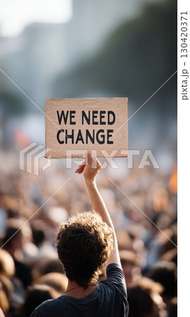 Activist holding a cardboard sign reading we need change during a bustling protest march, advocating passionately for vital political and social reforms in the community 130420371