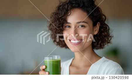 Happy young woman enjoying a healthy green smoothie or fresh juice, promoting wellness and a healthy lifestyle with a refreshing summer detox drink 130420598