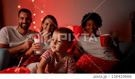 Family enjoying cozy movie night at home, with colorful snacks and drinks, surrounded by warm lighting and a relaxed atmosphere, creating joyful memories together 130420666