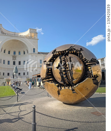 ROME, ITALY - AUGUST 02, 2025 Sphere Within Sphere (Sfera con Sfera) bronze sculpture by Arnaldo Pomodoro in the Vatican Museums, with Pinecone Fountain (Fontana della Pigna) in background 130420839