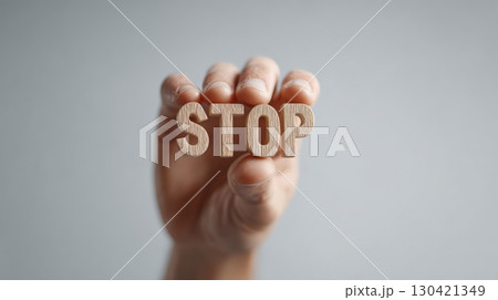 Hand holding wooden letters forming the word stop in front of a neutral background, possibly symbolizing a protest against immigration raids or other civil unrest 130421349