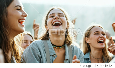 Group of young women laughing joyfully at an outdoor event, showcasing happiness and camaraderie, surrounded by friends enjoying a lively atmosphere with sunlight filtering through Group of young women laughing joyfully at an outdoor event, showcasing happiness and camaraderie, surrounded by friends enjoying a lively atmosphere with sunlight filtering through 130421612
