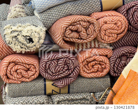 Rolled textiles with herringbone patterns in red, orange and gray stacked in a shop. Design, comfort and consumer choice represented through woven fabric, retail and cultural craft. Rolled textiles with herringbone patterns in red, orange and gray stacked in a shop. Design, comfort and consumer choice represented through woven fabric, retail and cultural craft. 130421878