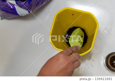 Yellow floral plastic flower pot being filled with soil using small trowel Yellow floral plastic flower pot being filled with soil using small trowel 130421891