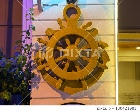 Anchor and helm symbol on a wall in warm evening light. Navigation, leadership and maritime heritage as a concept of direction, control and cultural identity. 130421903