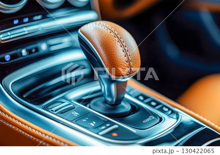 Detailed close up view of modern luxury car interior featuring brown leather automatic gear shifter with elegant stitching and control buttons. 130422065