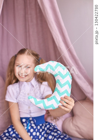 Smiling caucasian young girl in polka dot skirt holding chevron moon pillow 130422780
