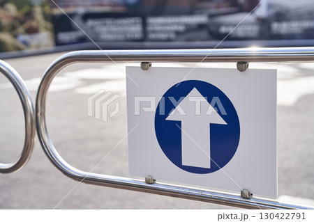 Blue upward arrow traffic sign on metal barrier indicating direction on a sunny 130422791
