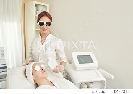 Caucasian female spa professional performing facial laser treatment on young Caucasian female spa professional performing facial laser treatment on young 130422810