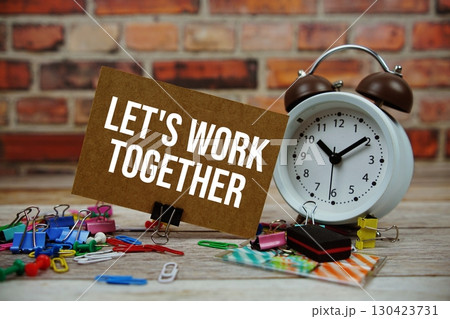 Let's Work Together text on paper card with alarm clock and stationary on wooden background 130423731
