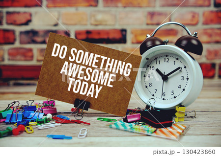 Do Something Awesome Today text on paper card with alarm clock and stationary on wooden background Do Something Awesome Today text on paper card with alarm clock and stationary on wooden background 130423860