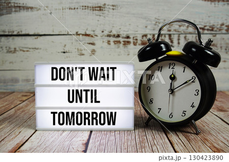 Don't Wait Until Tomorrow text on light box with alarm clock on wooden background 130423890