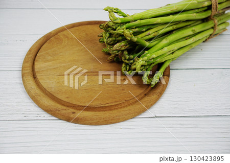 Bunch of fresh green asparagus stems with cutting wooden board on wooden background 130423895