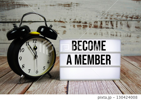 Become a Member text on light box with alarm clock on wooden background 130424008