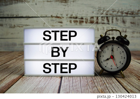 Step by Step text on light box with alarm clock on wooden background 130424013