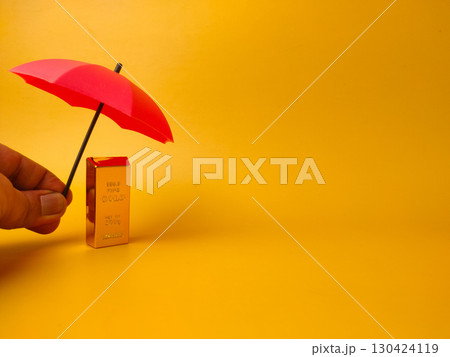Someone hand holding red umbrella covered gold bar on a yellow background with copy space. Someone hand holding red umbrella covered gold bar on a yellow background with copy space. 130424119