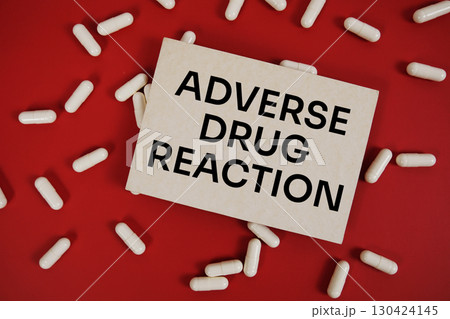 ADR Adverse Drug Reaction text written on paper card with medicine capsule on red background 130424145