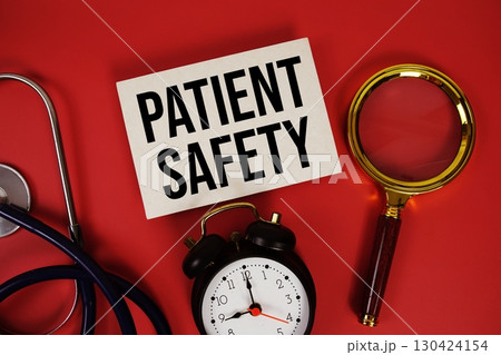Patient Safety text written on paper card with stethoscope, alarm clock and magnifying glass red background 130424154