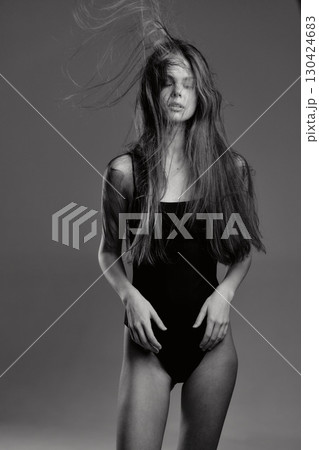 Black and white portrait of a woman with long hair in a dark outfit expressing emotion and movement. Black and white portrait of a woman with long hair in a dark outfit expressing emotion and movement. 130424683