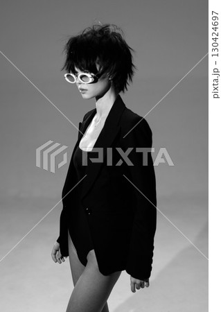 Black and white portrait of a stylish woman wearing a blazer and sunglasses in a minimalistic studio setting. Black and white portrait of a stylish woman wearing a blazer and sunglasses in a minimalistic studio setting. 130424697