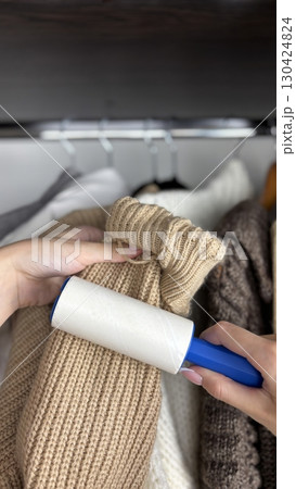 Woman using lint roller to clean lint laden clothes in closet, removing dust and debris from fabric. Wardrobe organization, clothing care, fashion and hygiene concept. Womens clothing maintenance Woman using lint roller to clean lint laden clothes in closet, removing dust and debris from fabric. Wardrobe organization, clothing care, fashion and hygiene concept. Womens clothing maintenance 130424824