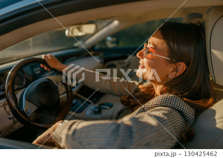 A Young Woman Happily Enjoying a Drive in a Luxurious and Stylish Car Beneath a Golden Sunset 130425462