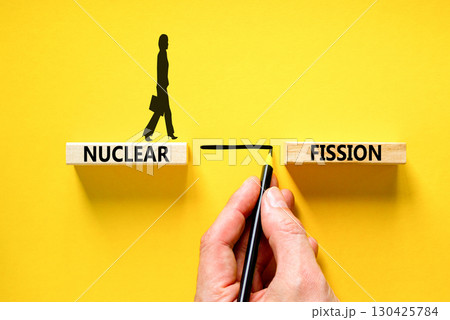Nuclear fission symbol. Concept words Nuclear fission on beautiful wooden blocks. Beautiful yellow table yellow background. Businessman hand. Business science nuclear fission concept. Copy space. 130425784