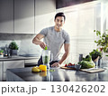 Smiling fit man preparing green smoothie with fruits and leafy vegetables in modern kitchen in bright natural light 130426202