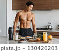 Shirtless fit man preparing healthy balanced breakfast with fresh juice and superfoods in modern kitchen 130426203
