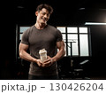 Smiling muscular man holding protein shaker in gym after workout session with fitness equipment in background 130426204