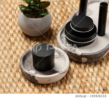 Black metal cosmetic jars and tubes on a decorative tray. Minimalism, skin care, stylish beauty background for brand presentation. Black metal cosmetic jars and tubes on a decorative tray. Minimalism, skin care, stylish beauty background for brand presentation. 130426218