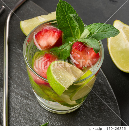 Refreshing mojito cocktail with lime, mint, strawberry, and ice on dark background, top view 130426226
