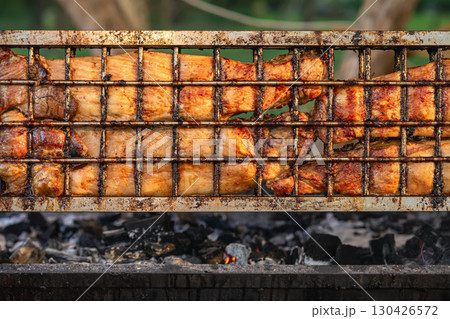 Juicy grilled meat sizzling on rotating hot barbecue grill with visible char marks and golden crust. Concept of grilled meat, outdoor barbecue, summer feast Juicy grilled meat sizzling on rotating hot barbecue grill with visible char marks and golden crust. Concept of grilled meat, outdoor barbecue, summer feast 130426572