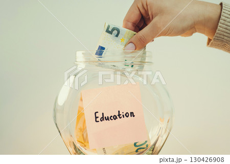 Saving up money for education concept. Hand putting 5 euro banknote to glass bank, toned image Saving up money for education concept. Hand putting 5 euro banknote to glass bank, toned image 130426908