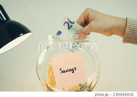Collecting savings from income concept, toned image. Person putting 20 euro banknote into the glass jar Collecting savings from income concept, toned image. Person putting 20 euro banknote into the glass jar 130426910