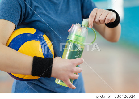 Female volleyball player opening water bottle on court. Young woman controlling water balance in the body during sport training 130426924