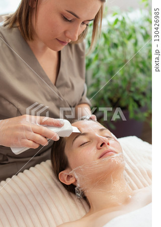Professional cosmetician doing ultrasound skin cleaning to female client. Modern ways to clean skin and look young and beautiful 130426985