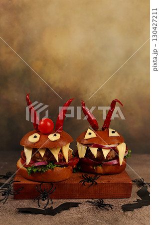 Horrible hamburgers with fresh lettuce, tomatoes, cream cheese, salad, onion, cutlets and peppers in the shape of horns on an old concrete background. Halloween food concept, cafe advertising, menu 130427211