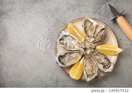 Fresh oysters with lemon wedges and oyster knife on plate top view, copy space Fresh oysters with lemon wedges and oyster knife on plate top view, copy space 130427412
