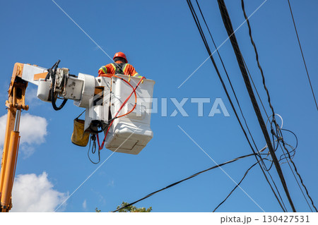 Electrical lineman in bucket truck working on power lines against blue sky Electrical lineman in bucket truck working on power lines against blue sky 130427531