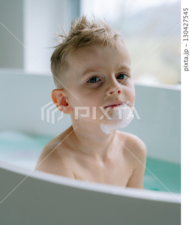 The boy soaks quietly in the modern white bathtub, surrounded by a serene, sunlit bathroom where soft light dances on the walls and polished fixtures. The boy soaks quietly in the modern white bathtub, surrounded by a serene, sunlit bathroom where soft light dances on the walls and polished fixtures. 130427545