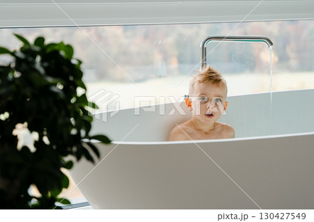 The boy, around five years old, laughs as he creates little waves with his toy boat, the spacious white tub around him shimmering with turquoise water under the daylight. High quality photo The boy, around five years old, laughs as he creates little waves with his toy boat, the spacious white tub around him shimmering with turquoise water under the daylight. High quality photo 130427549