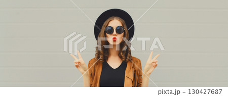 Portrait of beautiful young woman blowing kiss, stylish girl in black hat posing on gray background Portrait of beautiful young woman blowing kiss, stylish girl in black hat posing on gray background 130427687