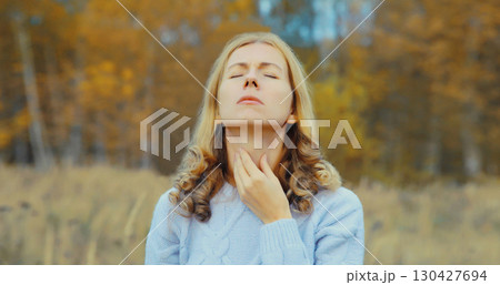 Sick exhausted woman suffering from acute sore in throat flu, touches neck with hand outdoor in park 130427694