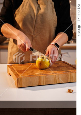 Woman slicing a yellow apple on a wooden board in warm kitchen light 130428128