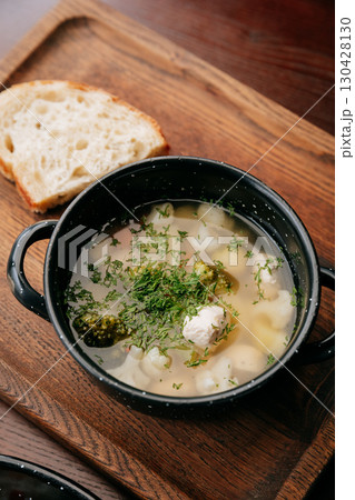 Clear soup with vegetables and chicken meatballs, served with rustic bread on wooden tray 130428130
