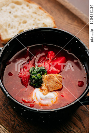 Traditional Ukrainian borscht with sour cream, pork, and fresh herbs in a black rustic bowl 130428134
