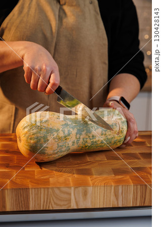 Close-up of hands cutting squash on wooden board in cozy kitchen setting 130428143