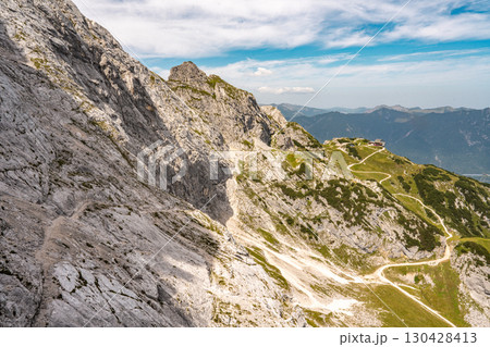 Hiking Trail From Alpspitze Via Ferrata In The Bavarian Alps: Scenic Mountain Path With Rocky Slopes And Green Valleys Under Clear Blue Sky 130428413